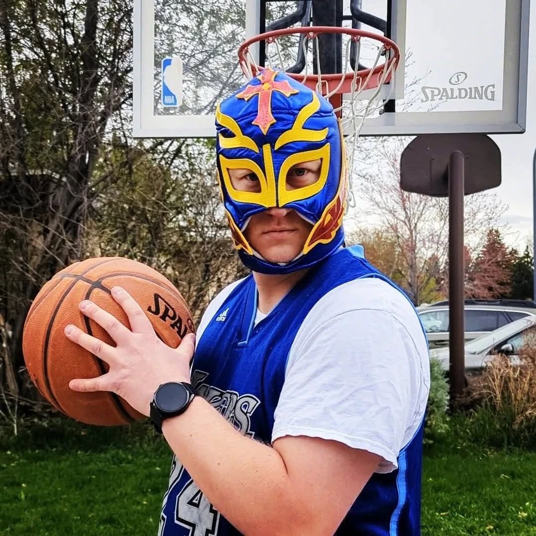 A man holding a basketball wearing a Kobe Bryant Lakers jersey with a luchador mask